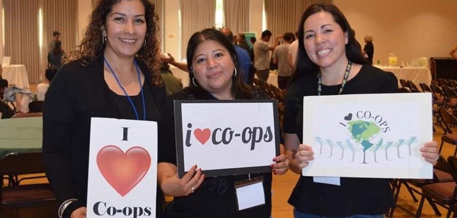 Three women holding signs that promote co-ops